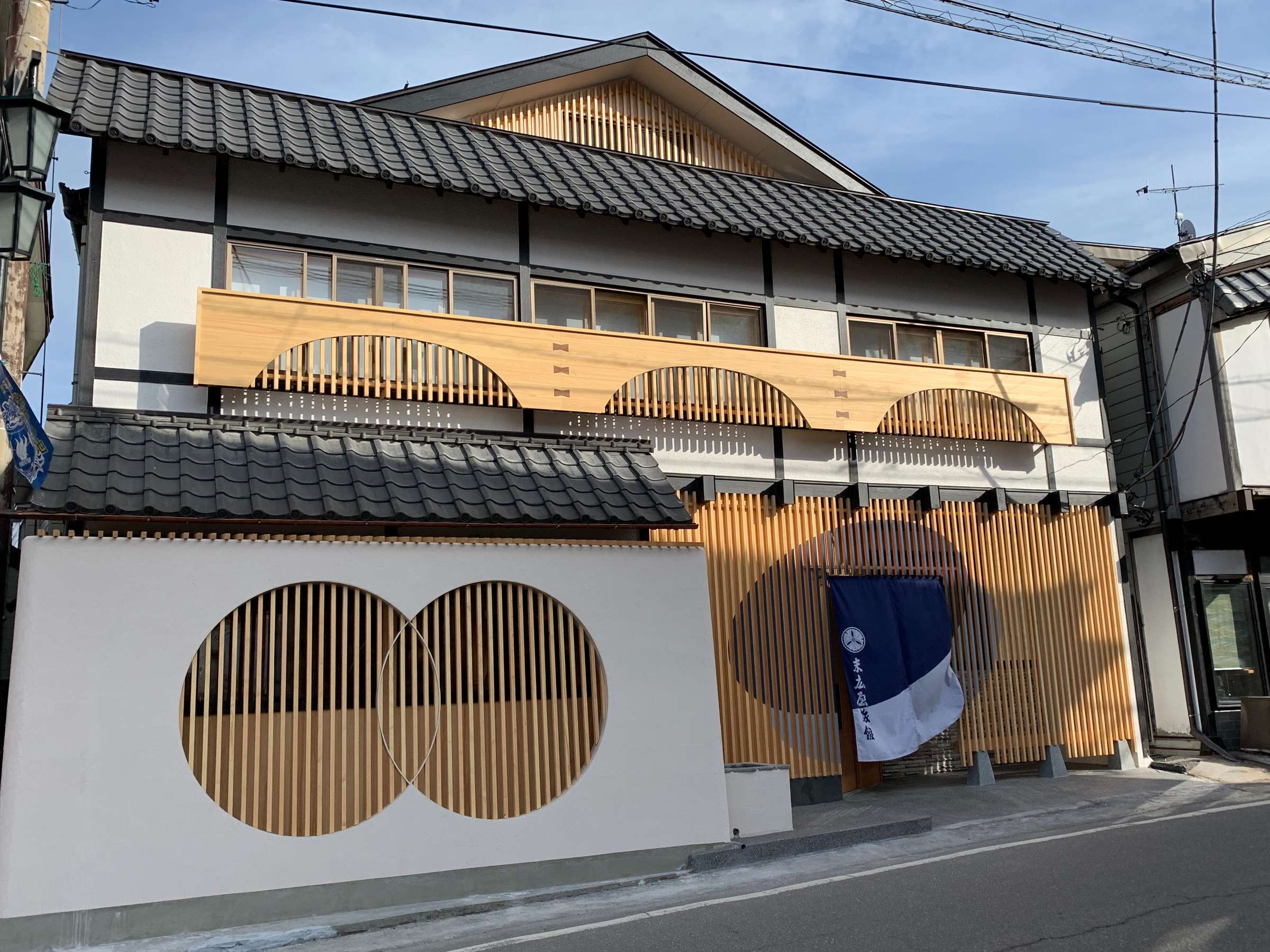 Renovated street facade of Suehiroya Ryokan in Kusatsu Onsen with a tile roof, cedar lattice screens and an indigo entrance noren curtain