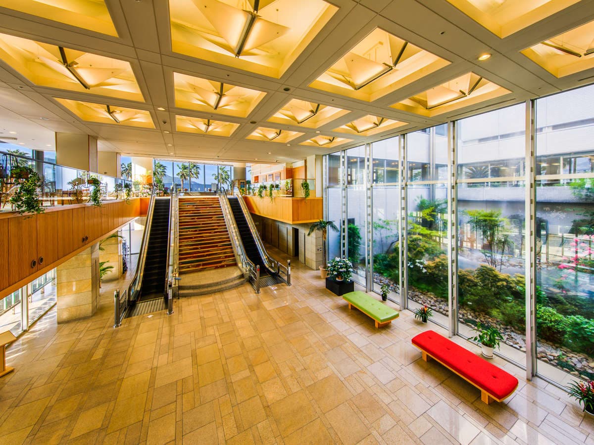 Bright multi-story atrium lobby with escalators and glass walls onto the garden