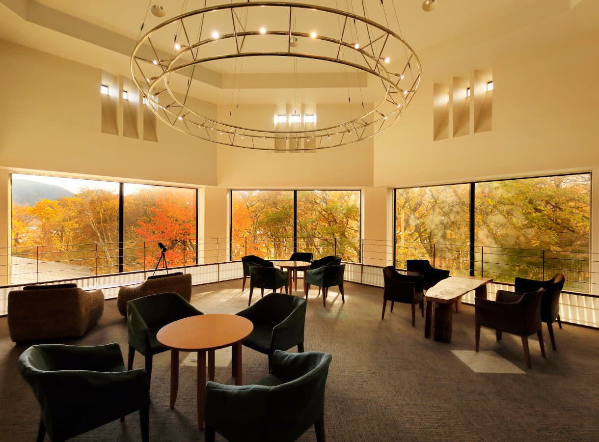 Spacious lounge with circular chandelier and floor-to-ceiling windows framing autumn foliage at Okunikko Hotel Shikisai