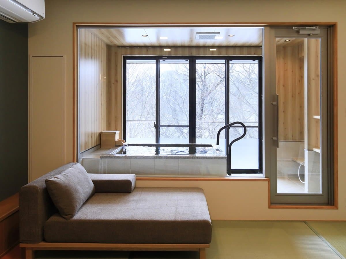 Modern guest room with a granite in-room bath and sofa facing snow-covered trees at Okunikko Hotel Shikisai