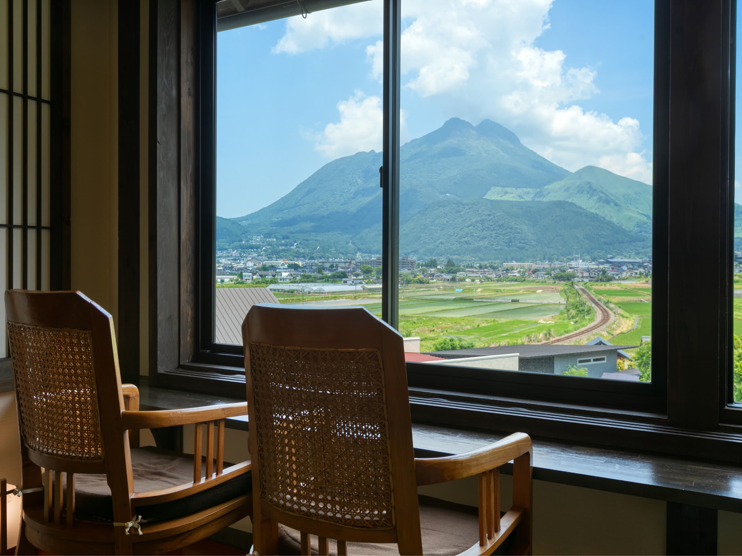Guest room at Tosyoan, Yufuin Onsen, with rattan chairs framing a window view of Mount Yufu and the rice fields