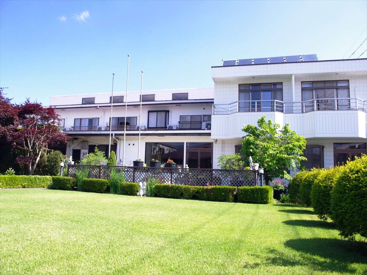 Full exterior of K's House Fuji View hostel with a wide green lawn garden under blue sky