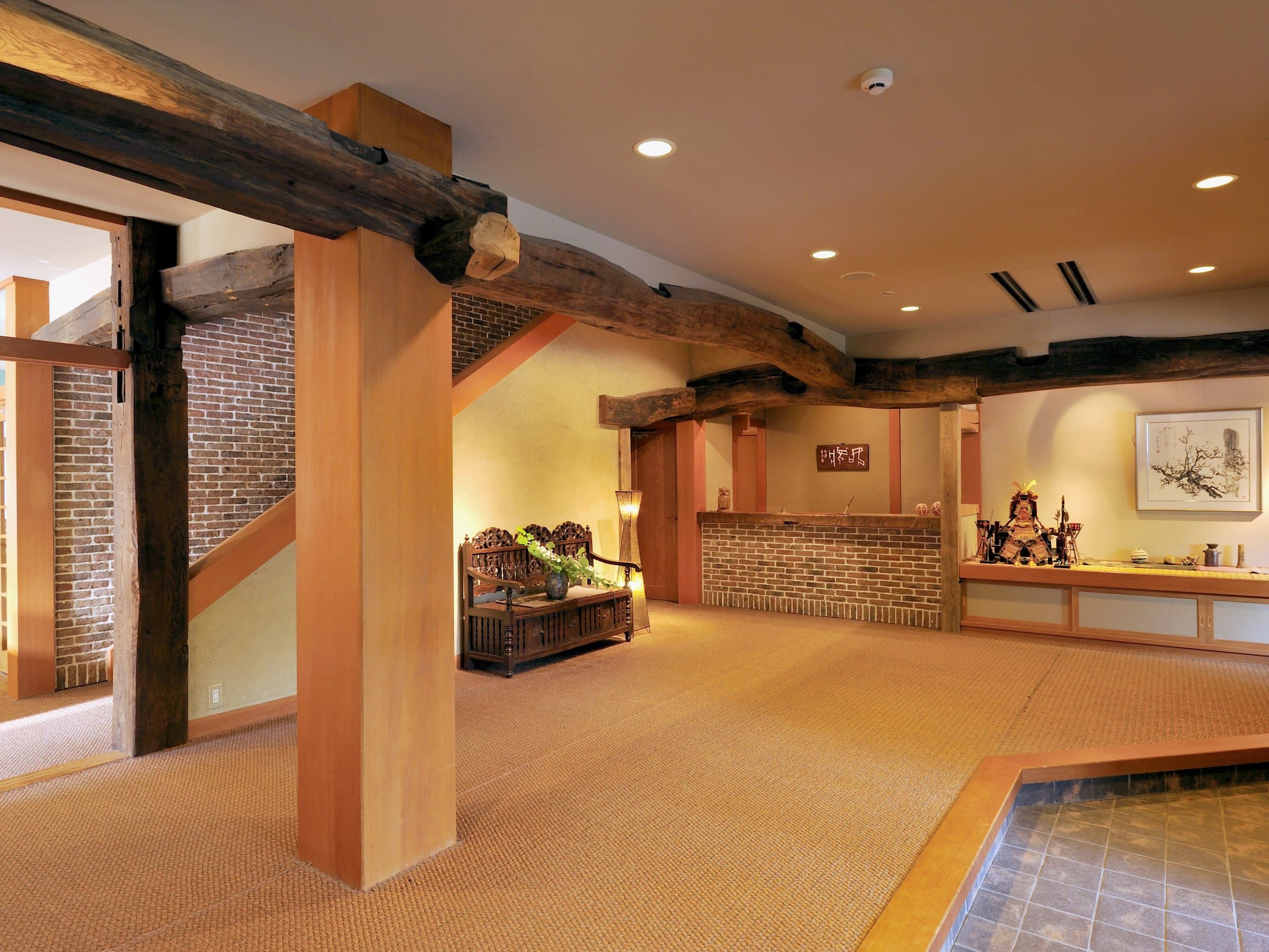 Shirouma-so lobby interior with exposed timber beams, brick accents and tatami-matted flooring in Hakuba Onsen