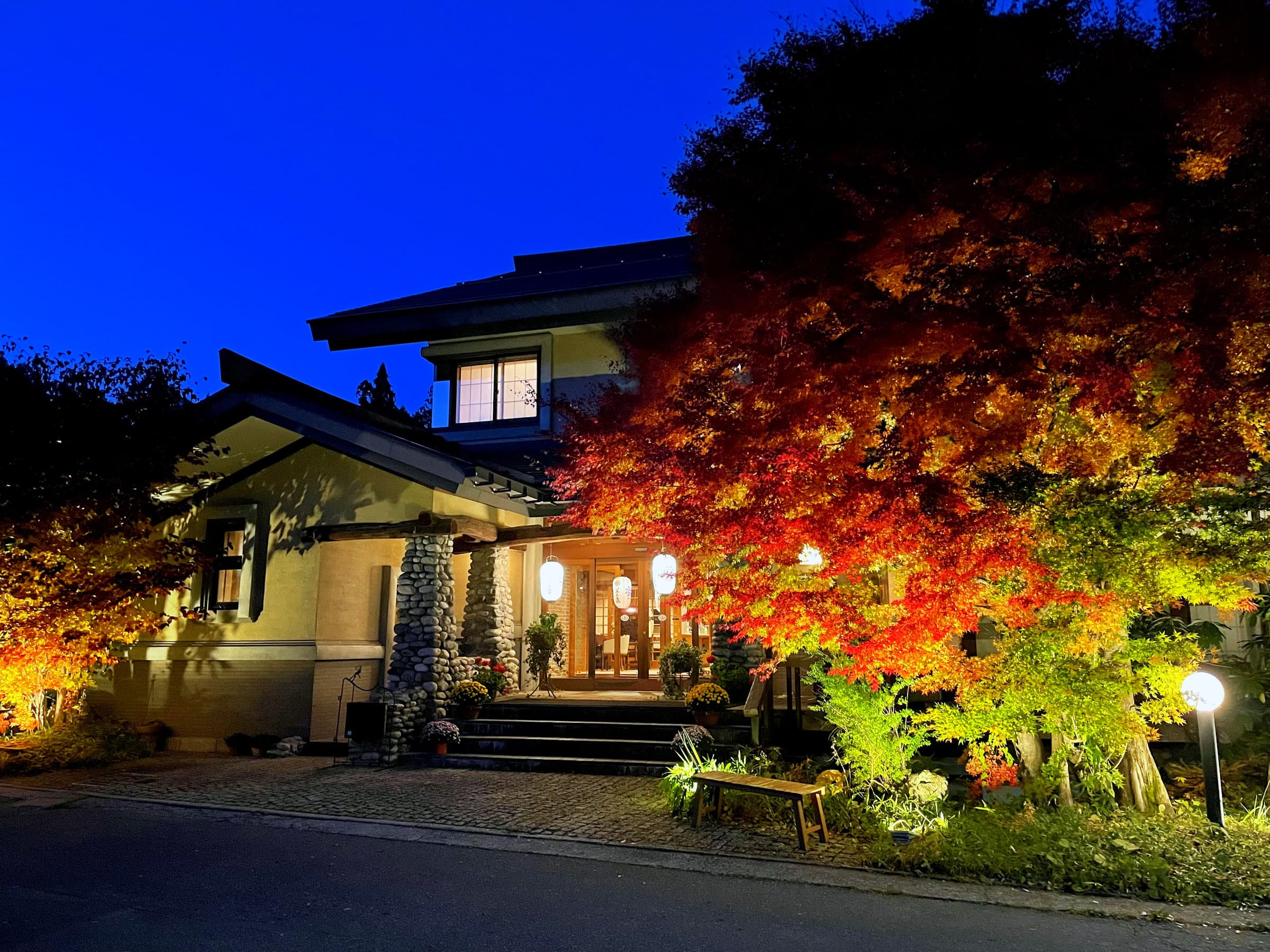 Shirouma-so main building illuminated at night with golden entrance lights and autumn foliage in Hakuba Onsen