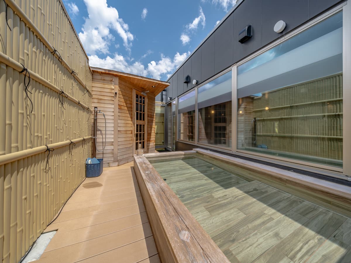 Rooftop terrace at Wat Hotel & Spa Hida Takayama with a fire-pit lounge, cypress bath house and mountain views under blue sky