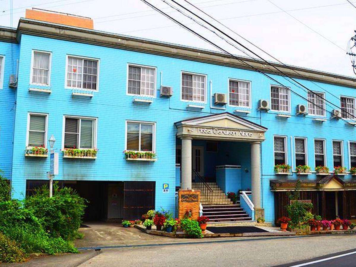 Daylight view of Hotel Cerulean Alpen's bright blue facade and flower-lined entrance in Tsugaike, Hakuba