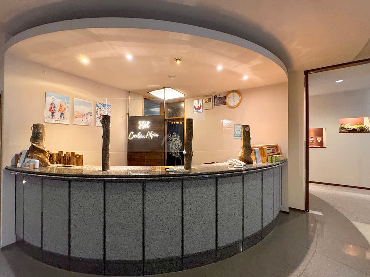 Curved stone front-desk and reception area with mountain prints at Hotel Cerulean Alpen, Hakuba
