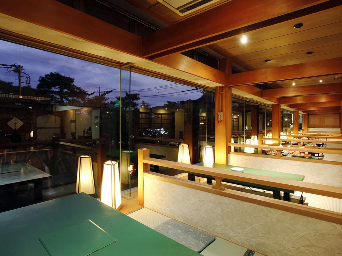 Warm wood-and-glass dining hall with private booths and an evening river view at Kinugawa Park Hotels