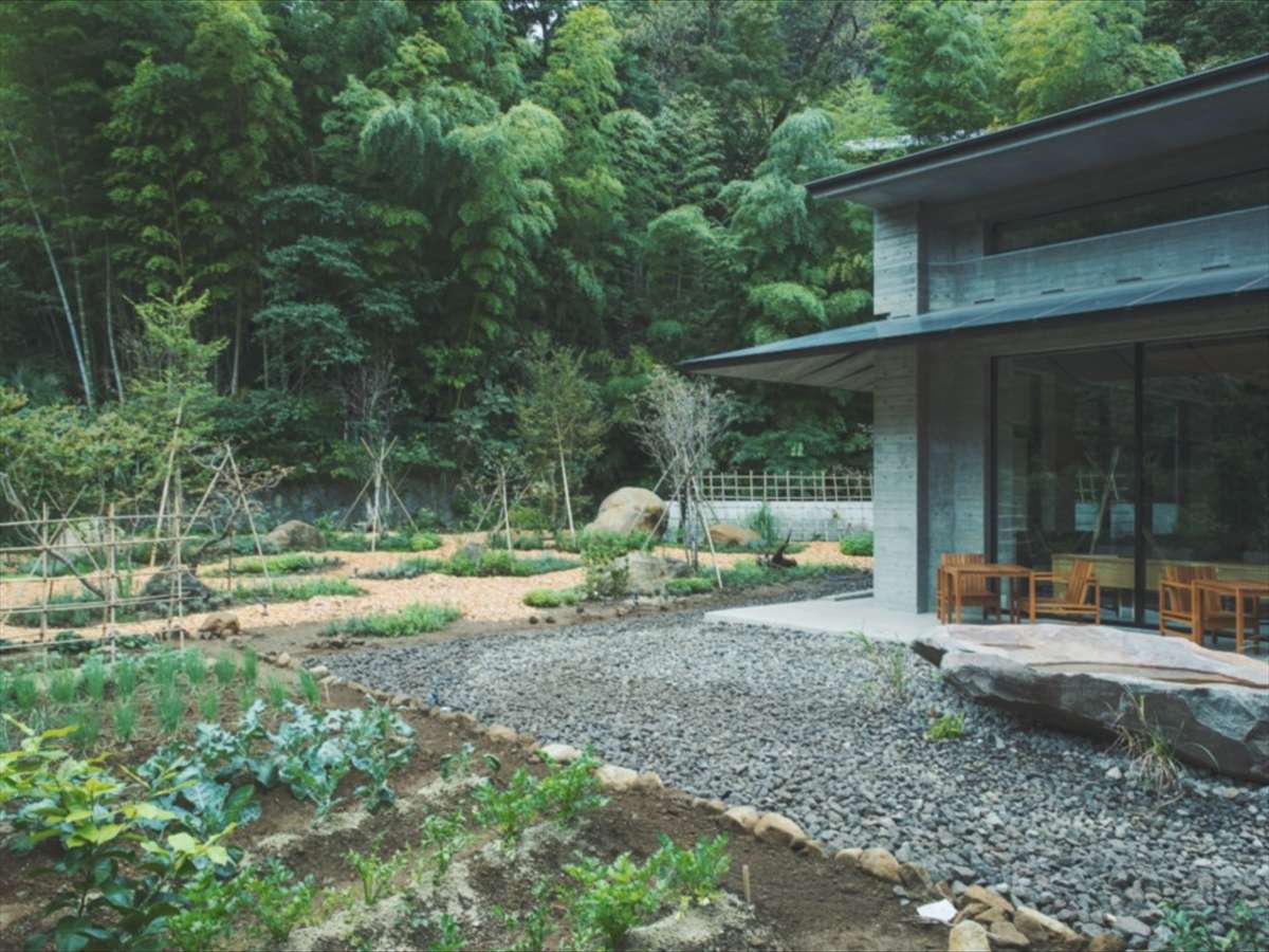 SOKI ATAMI concrete pavilion with terrace seating beside a kitchen garden and forested hillside in Atami Onsen
