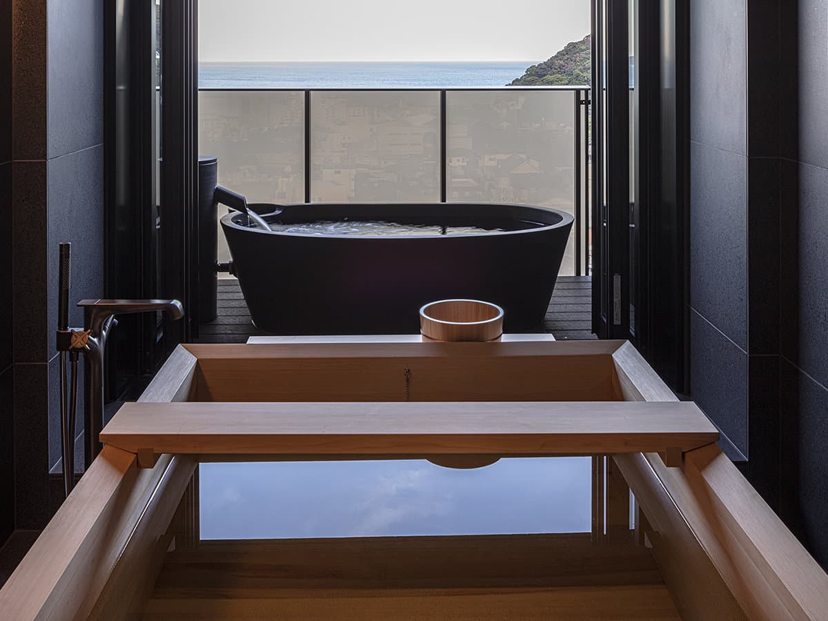 Private in-room cypress and stone bath at SOKI ATAMI overlooking the sea and townscape of Atami