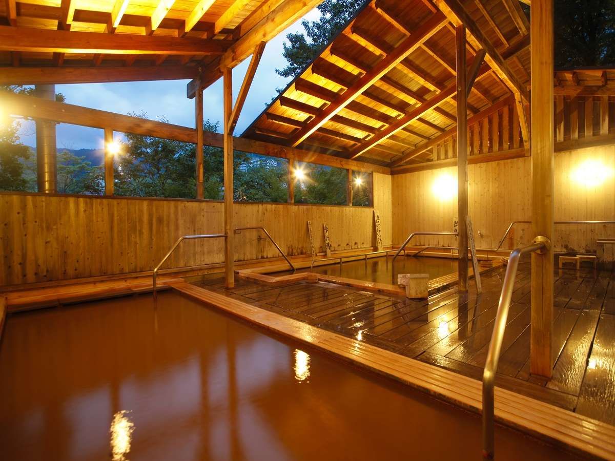 Covered kinsen iron-spring rotenburo at Spa Terrace Shisui with reddish-brown mineral water glowing under timber rafters at dusk