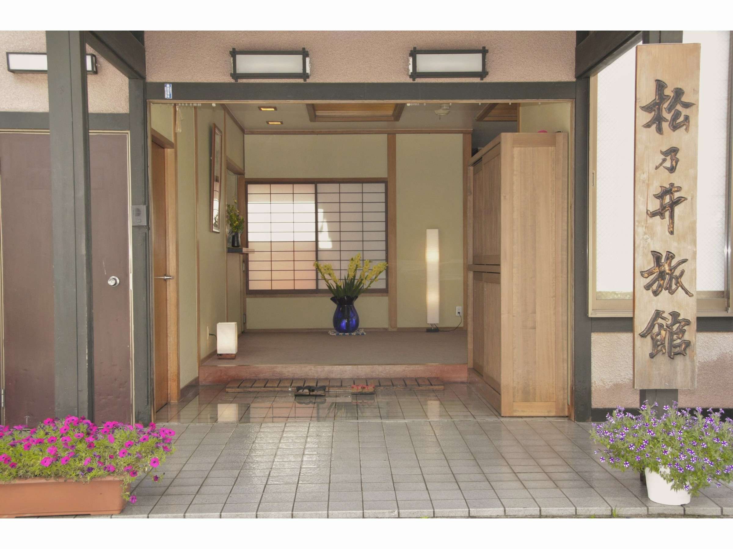 Ryokan entrance with open wooden doors leading to a tatami genkan and flower planters