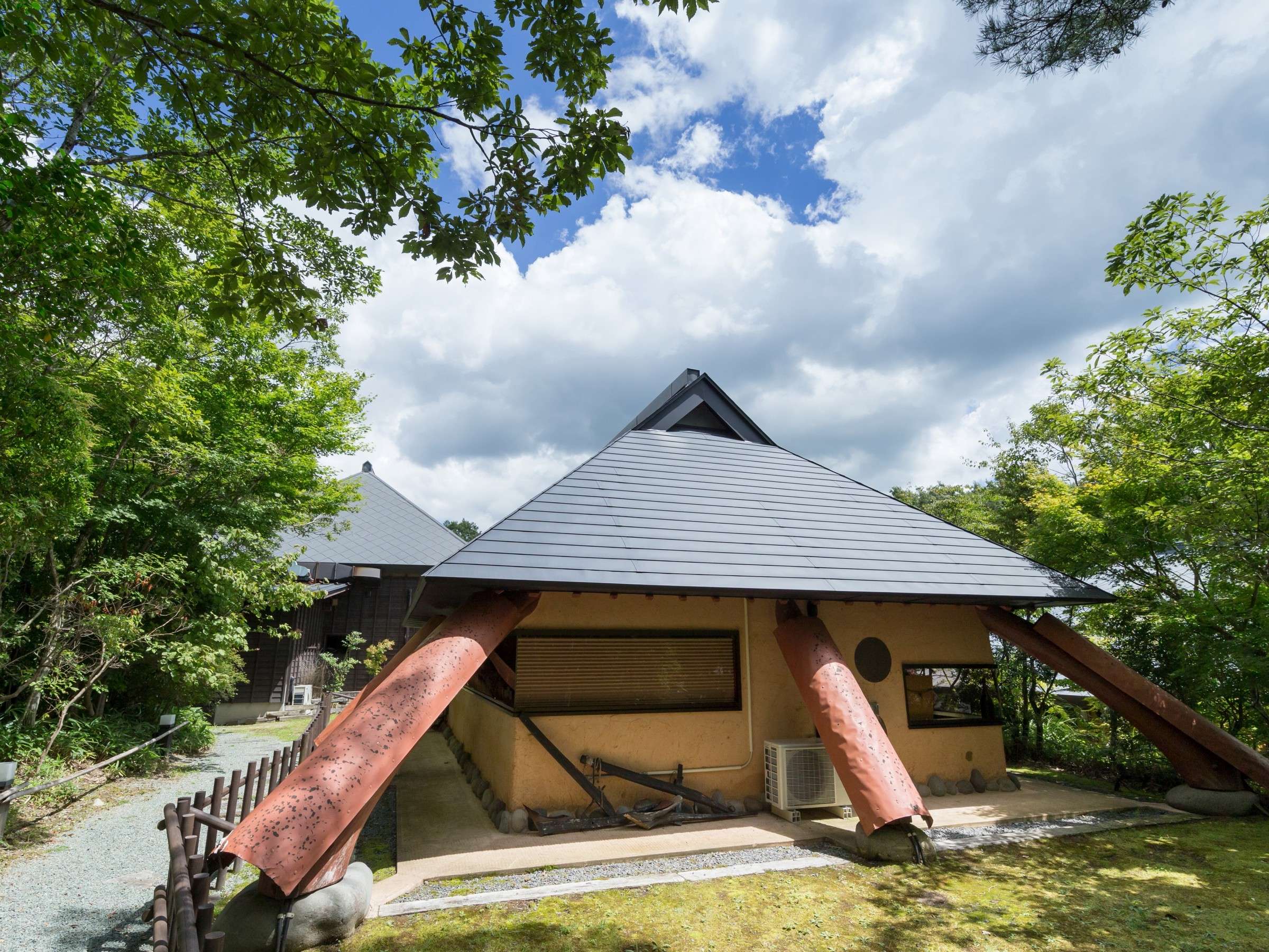 Satonoyu Waraku detached lounge building exterior with dark hipped roof under a blue sky surrounded by trees