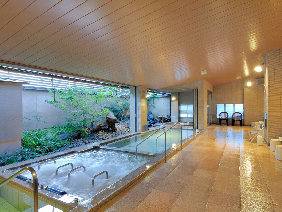 Spacious indoor public bath with a planted garden view at Kanazawa Manten Hotel Ekimae