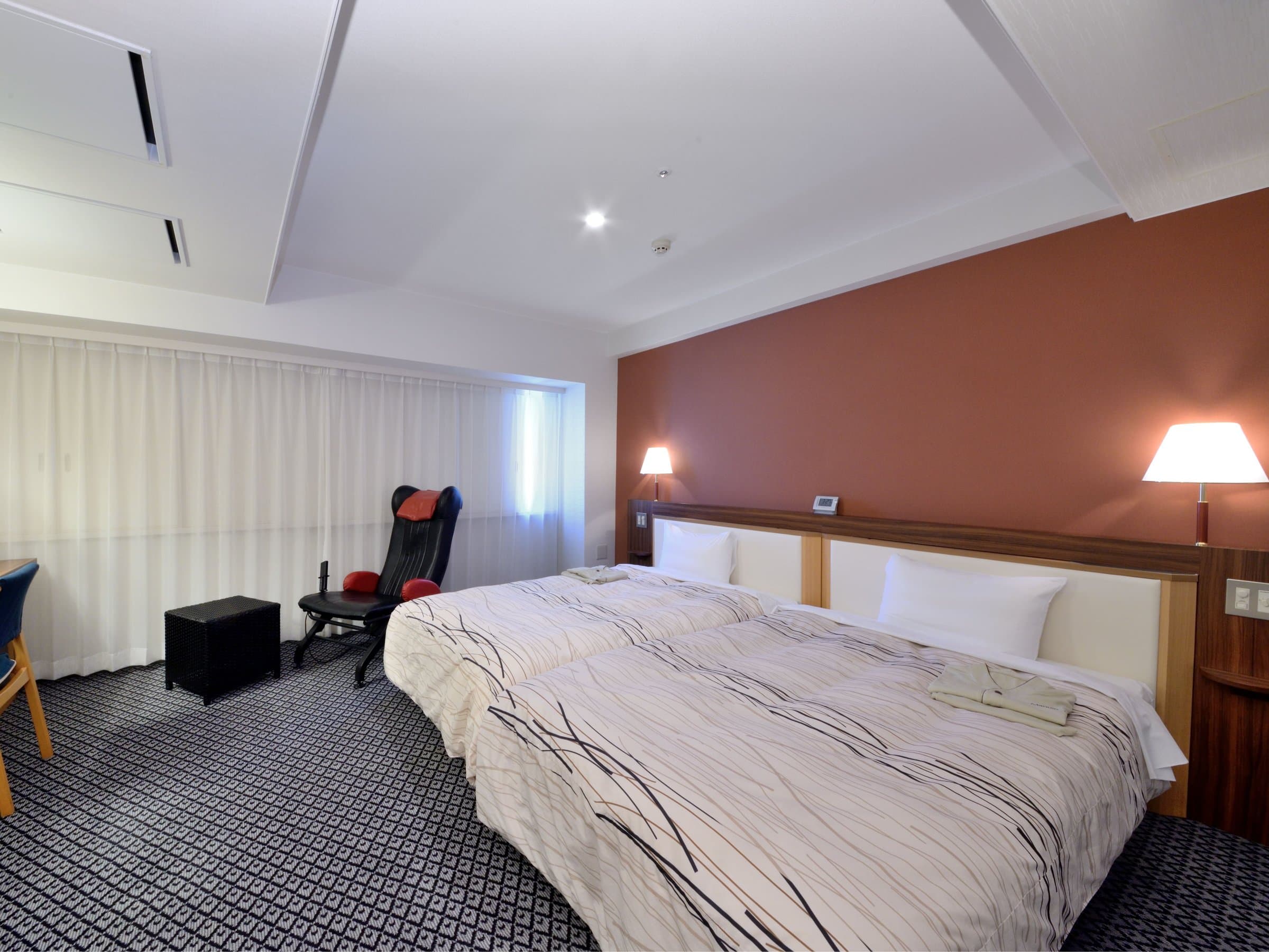 Twin guest room with rust accent wall, reclining chair and patterned carpet at Kanazawa Manten Hotel Ekimae
