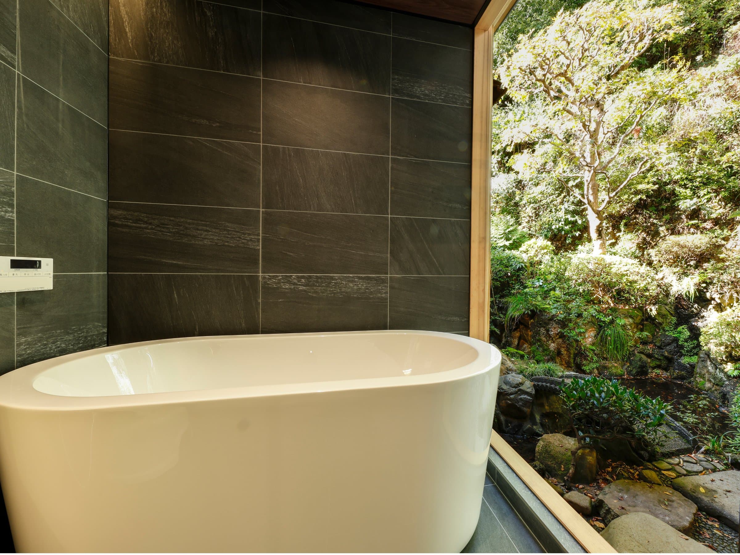 Private stone soaking tub beside a picture window framing a green forested garden, Yamamotoya, Kinosaki Onsen