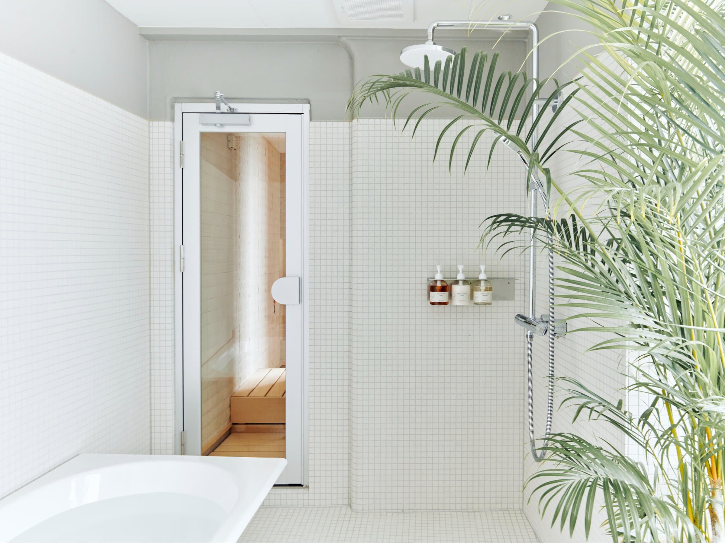 Bright white-tiled spa bathroom at Korinkyo Kanazawa with a rain shower, deep tub and a sauna cabin beyond