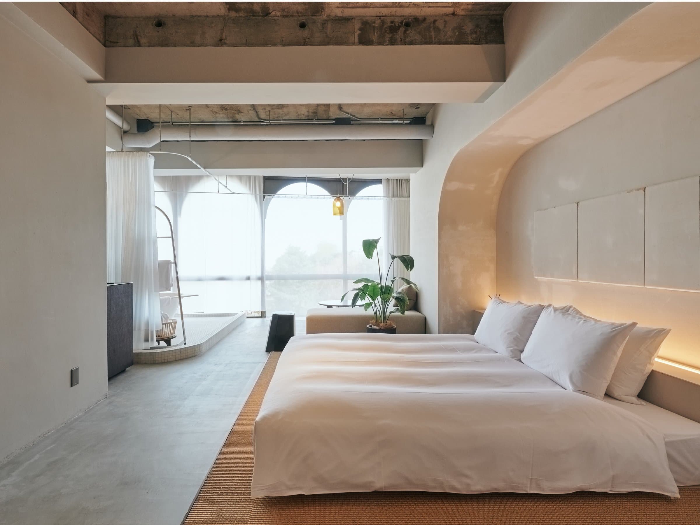 Premium guest room at Korinkyo Kanazawa with low bed, in-room bath behind sheer curtains and arched windows letting in daylight