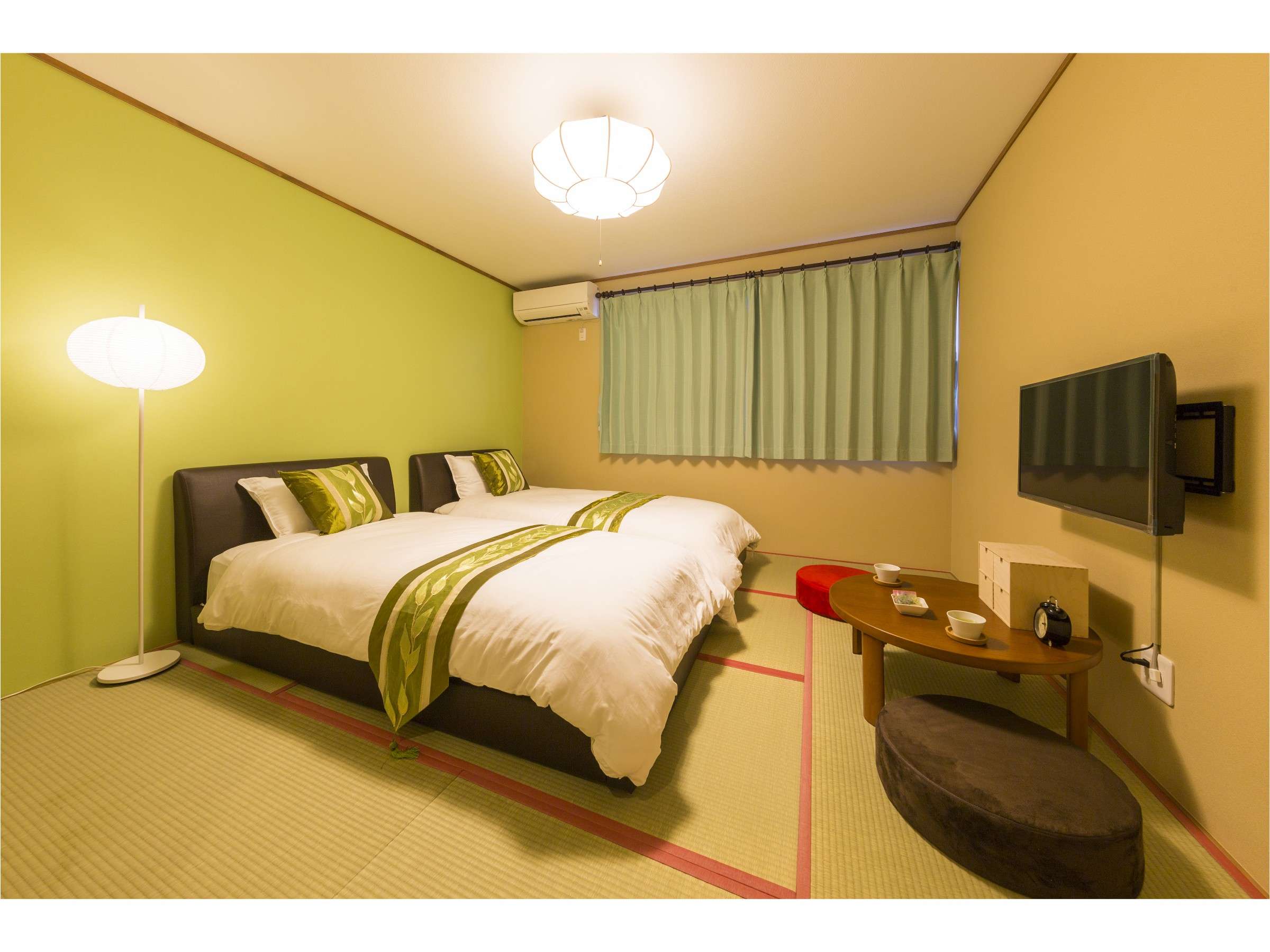 Twin-bed tatami guest room with bright green accent wall, paper floor lamp and low wooden table