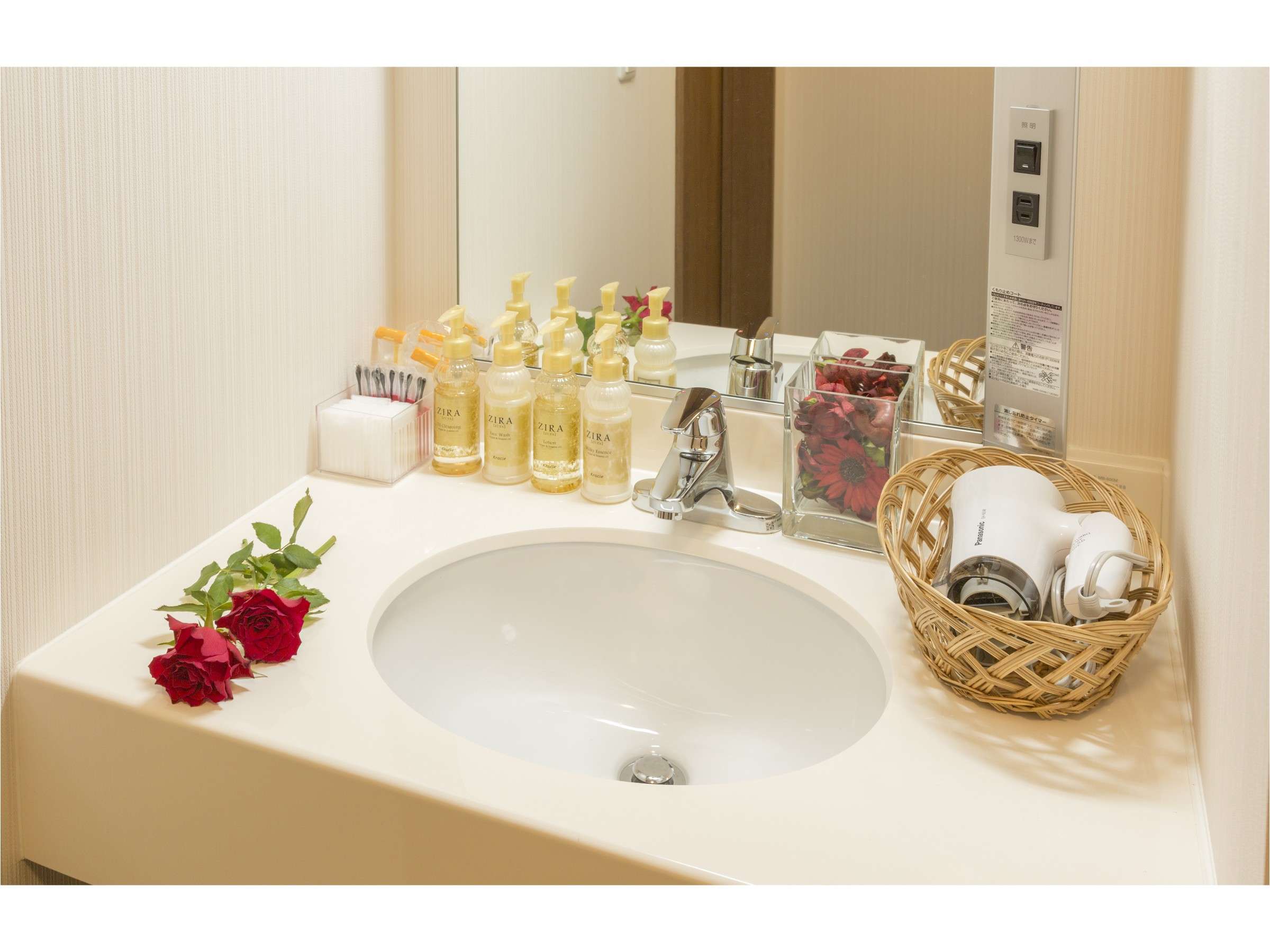 Clean vanity sink with amenity bottles, a hairdryer in a wicker basket and fresh red roses