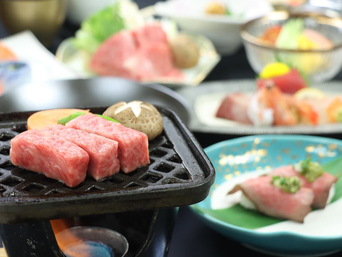 Marbled Hida wagyu beef grilling on a tabletop hibachi with seasonal sides at Ryokan Tanabe