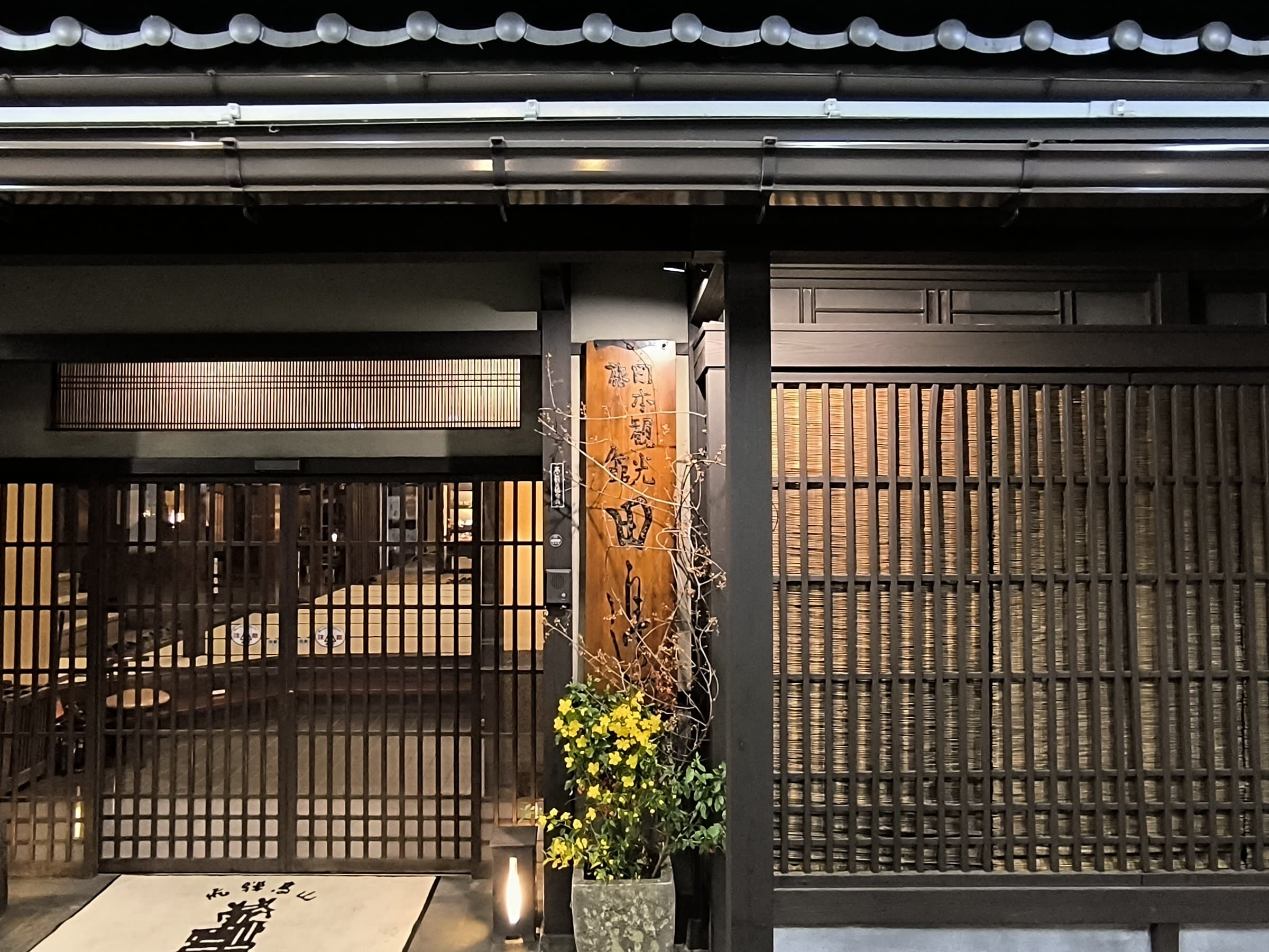 Ryokan Tanabe traditional wooden facade and lattice entrance lit at dusk in Takayama old town