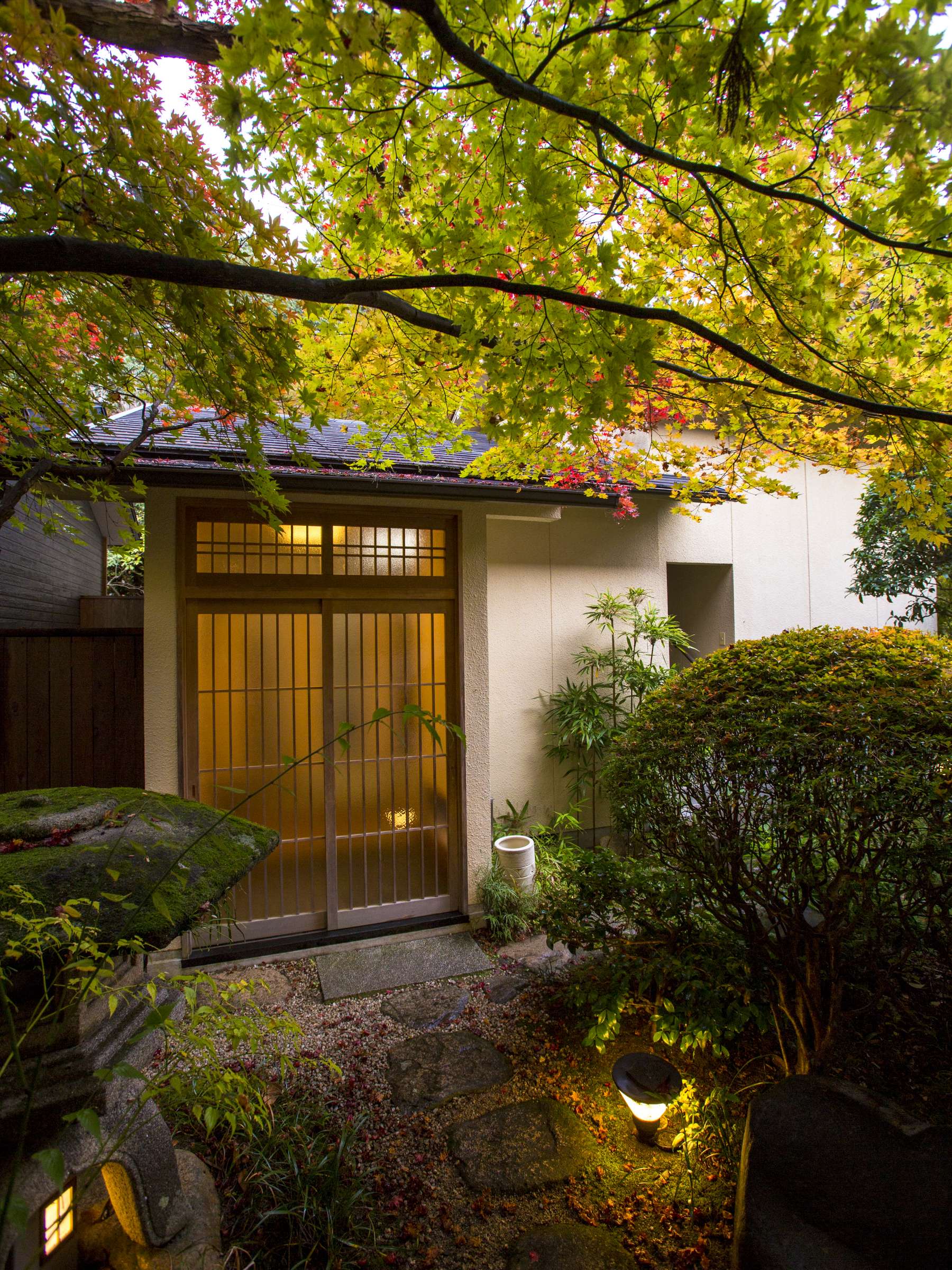 Lantern-lit entrance gate and sliding-door genkan of Hashinoya Bekkan Ransui at dusk, set on a mossy stone path beneath a maple tree