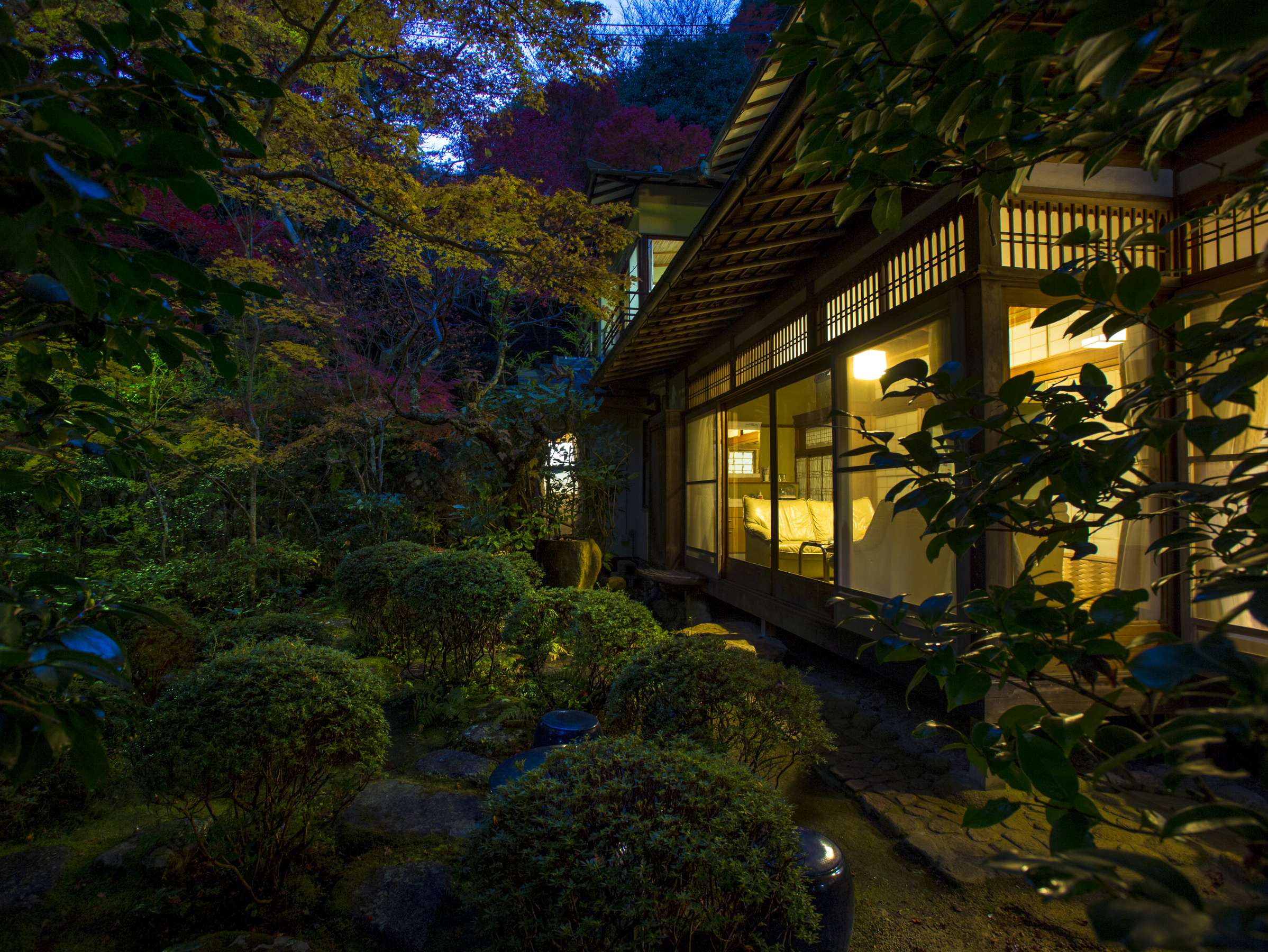 Hashinoya Bekkan Ransui's wooden villa glowing from within at night, viewed across its softly lit autumn garden with clipped shrubs and stone path