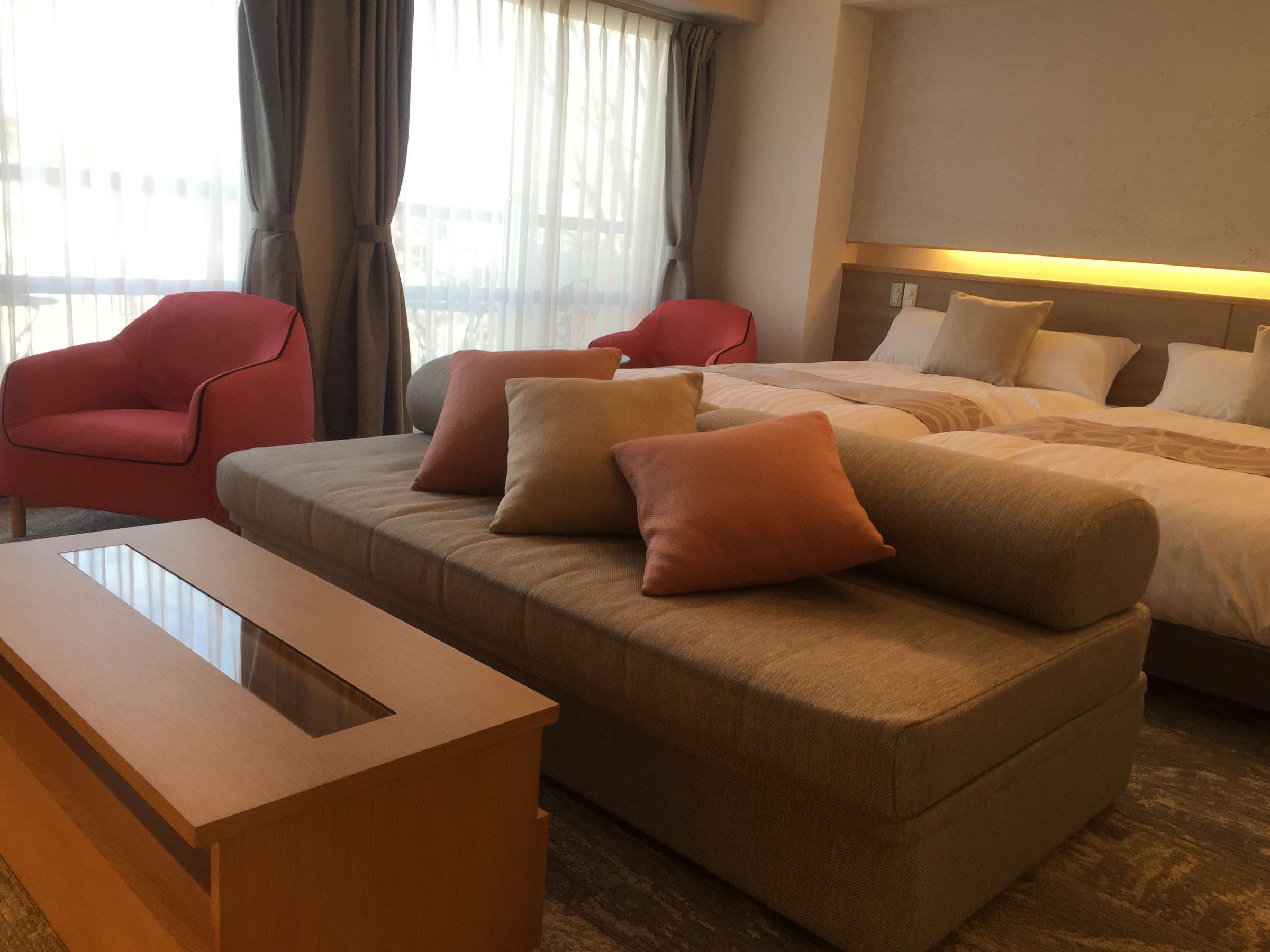 Western-style twin room with daybed sofa and red accent armchairs by a curtained window at Hotel Spax Kusatsu