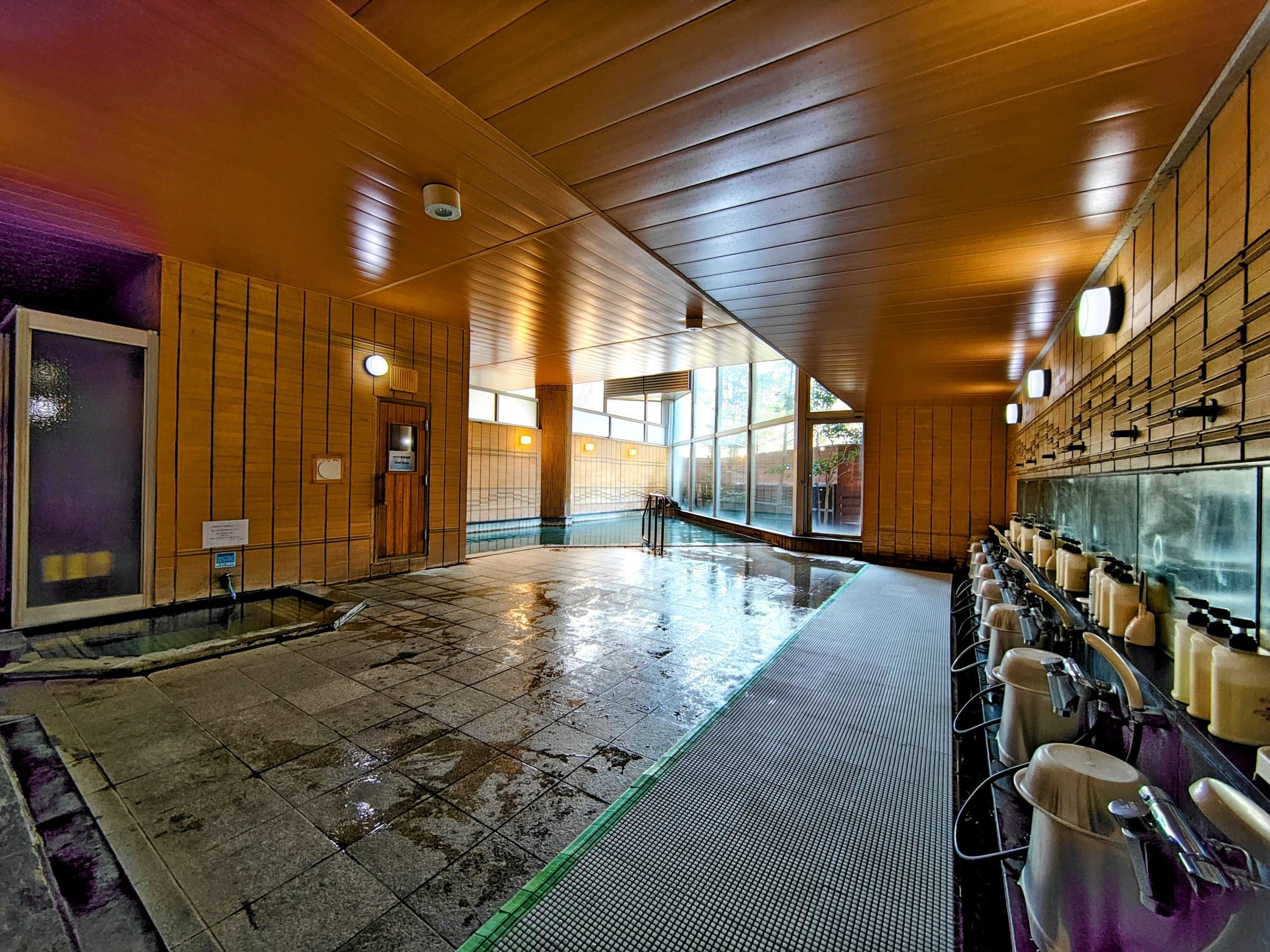 Spacious indoor onsen bath hall with stone floor, wash stations and wide windows at Hotel Spax Kusatsu