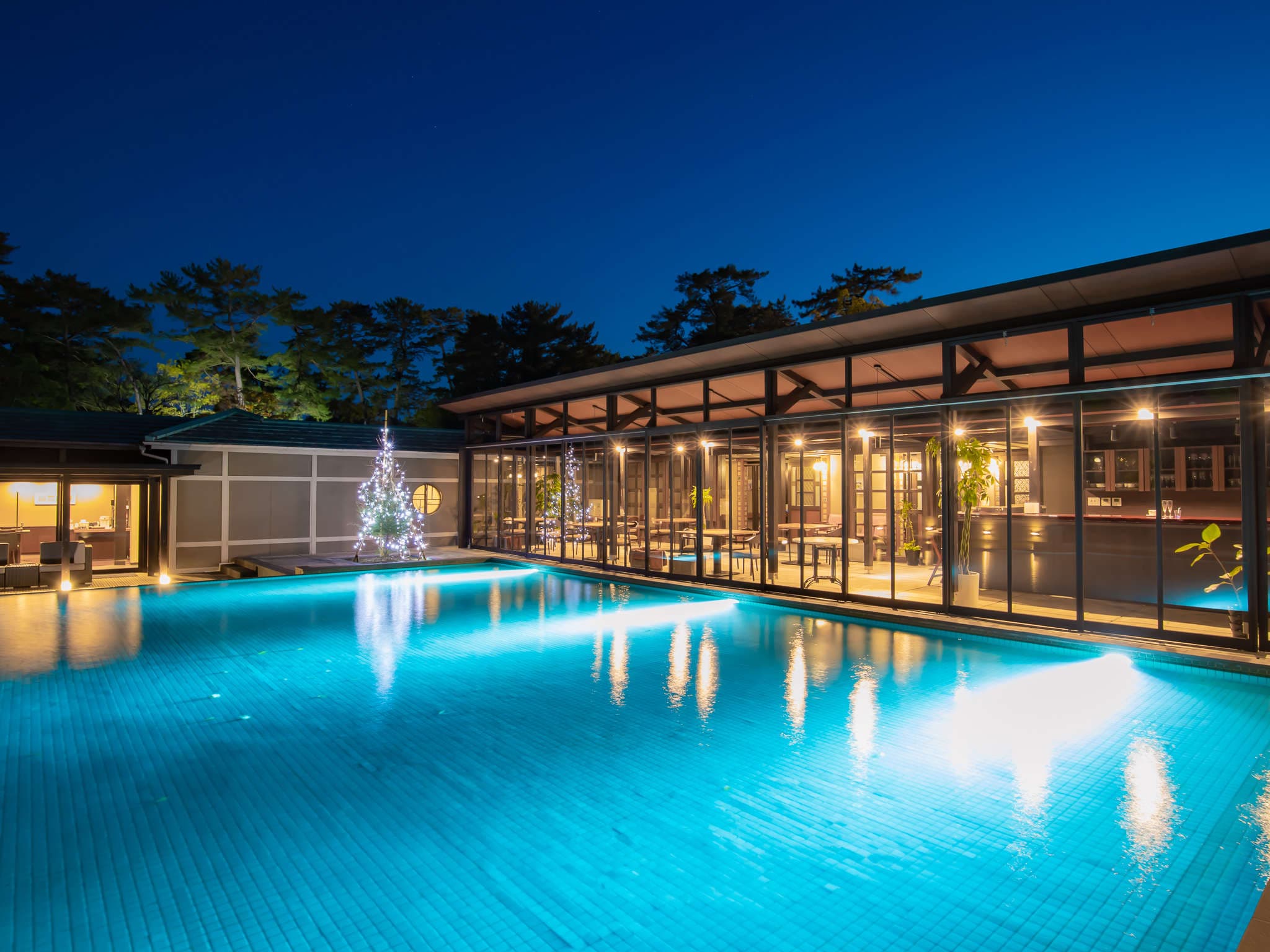 Night view of the outdoor pool glowing turquoise beside an illuminated decorative tree and glass lounge, Amane Resort GAHAMA, Beppu Onsen