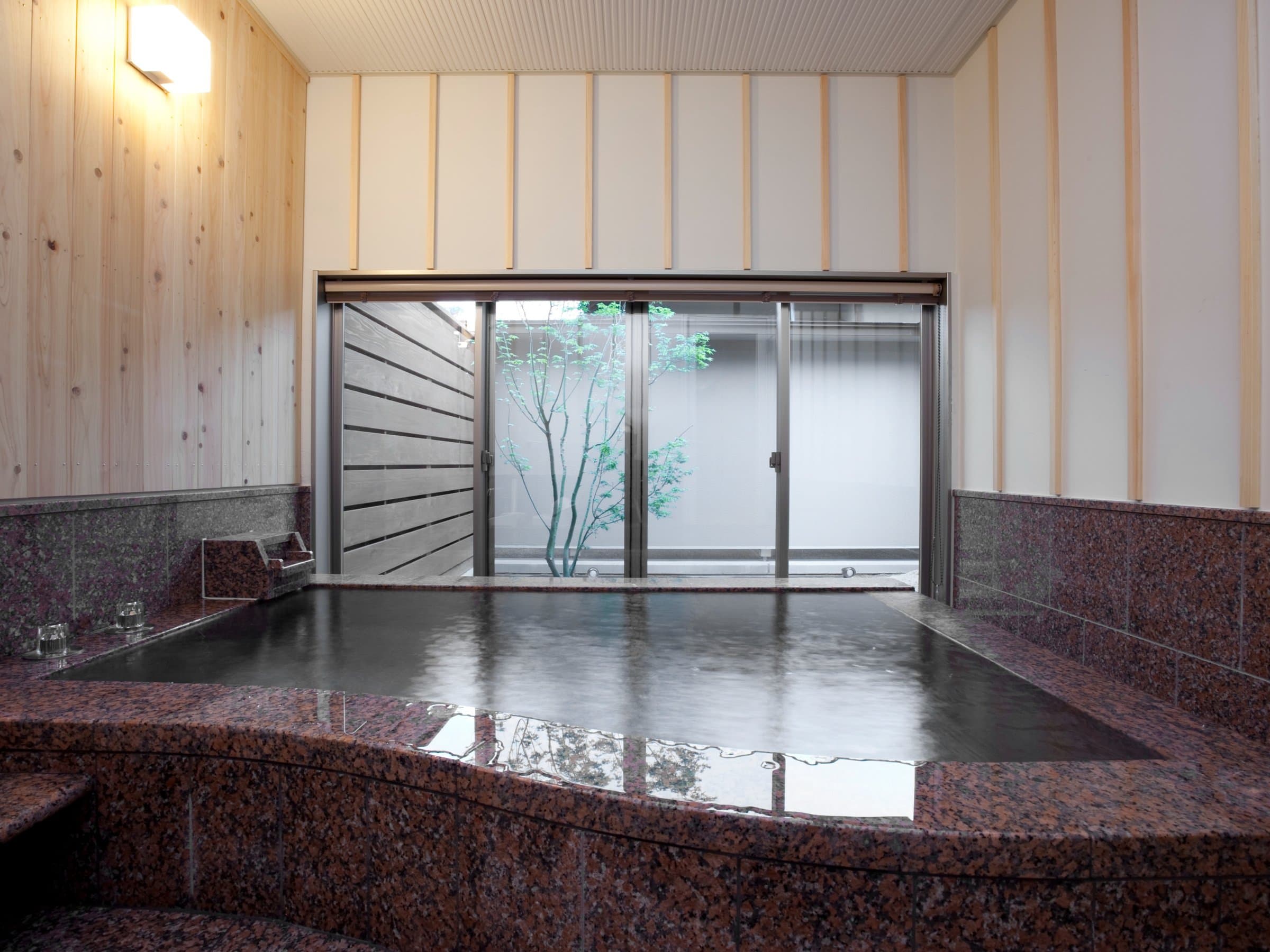Indoor hot spring bath with polished granite tub and cedar walls opening to a small garden, Amane Resort GAHAMA, Beppu Onsen