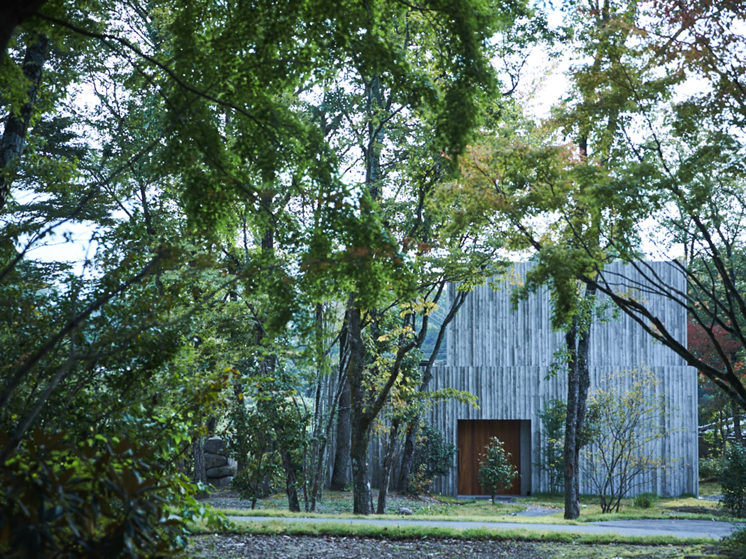 Modern wood-and-concrete guest villa of Sanso Warabino set among lush forest trees in Yufuin