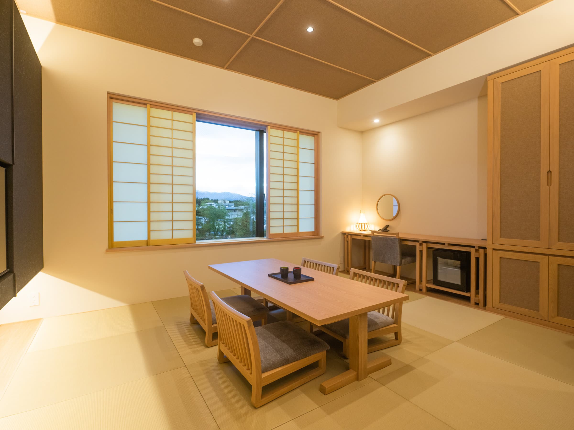 Tatami guest room with low wooden table, chairs and a wide window framing a mountain view
