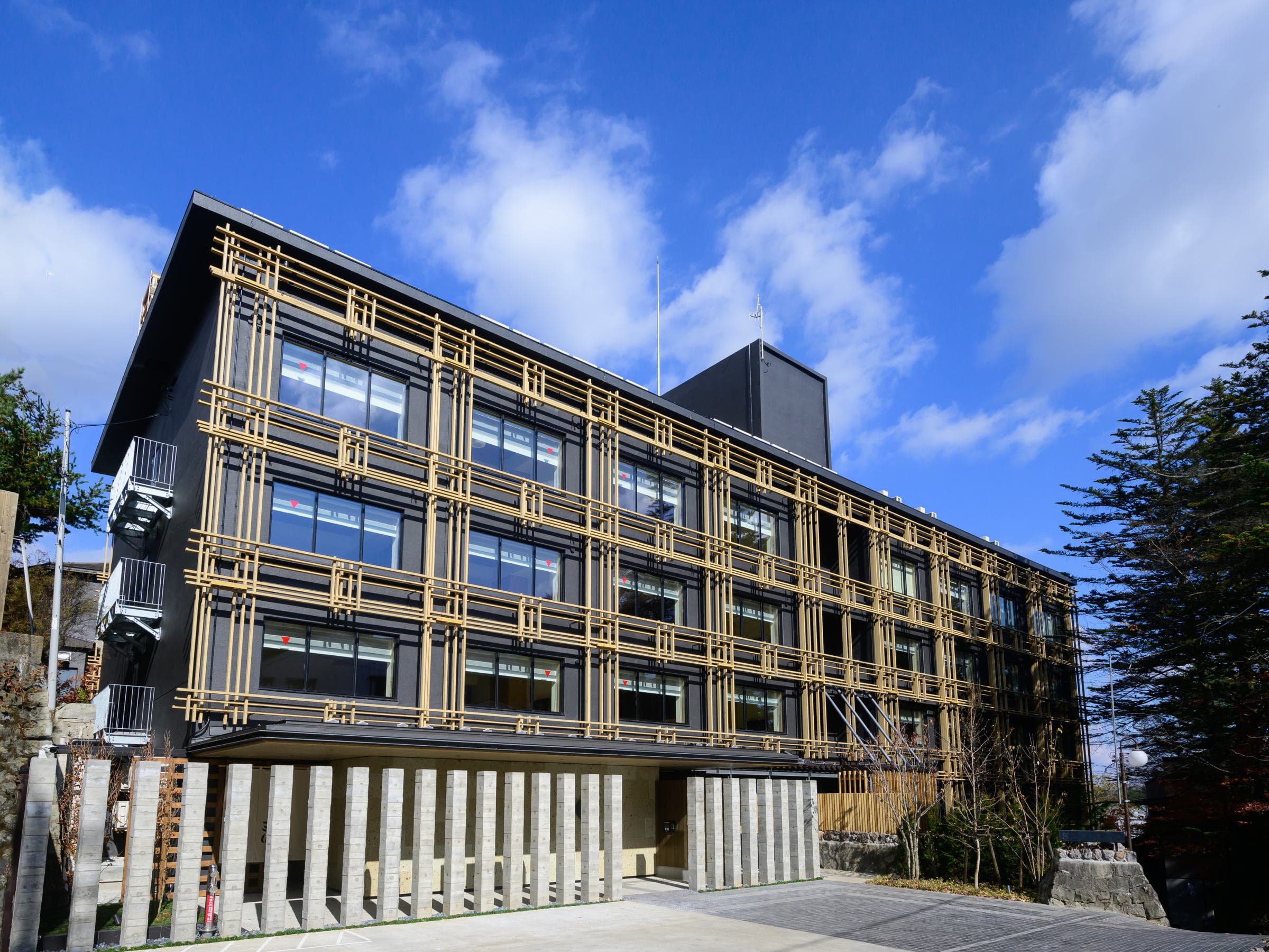Modern dark-timber ryokan building with golden lattice facade under a blue sky