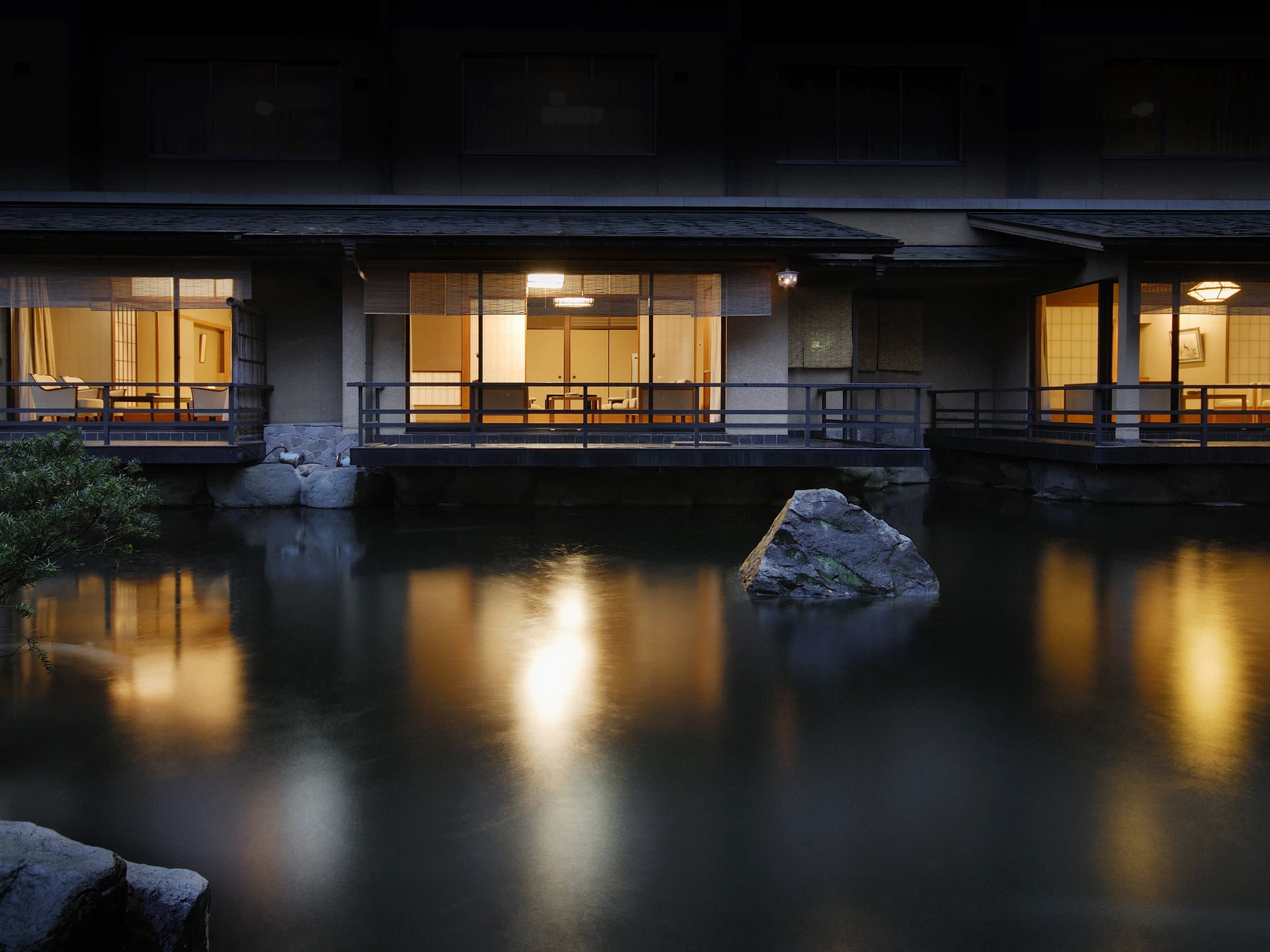 Riverside guest-room facade glowing warmly at dusk above a still reflecting pond, Suimeikan, Gero Onsen