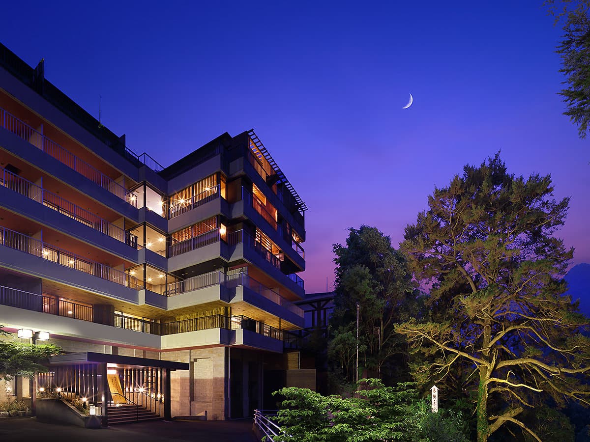 Hotel Tsuga no Ki exterior glowing at dusk under a crescent moon with lit guest-room balconies in Kinugawa Onsen