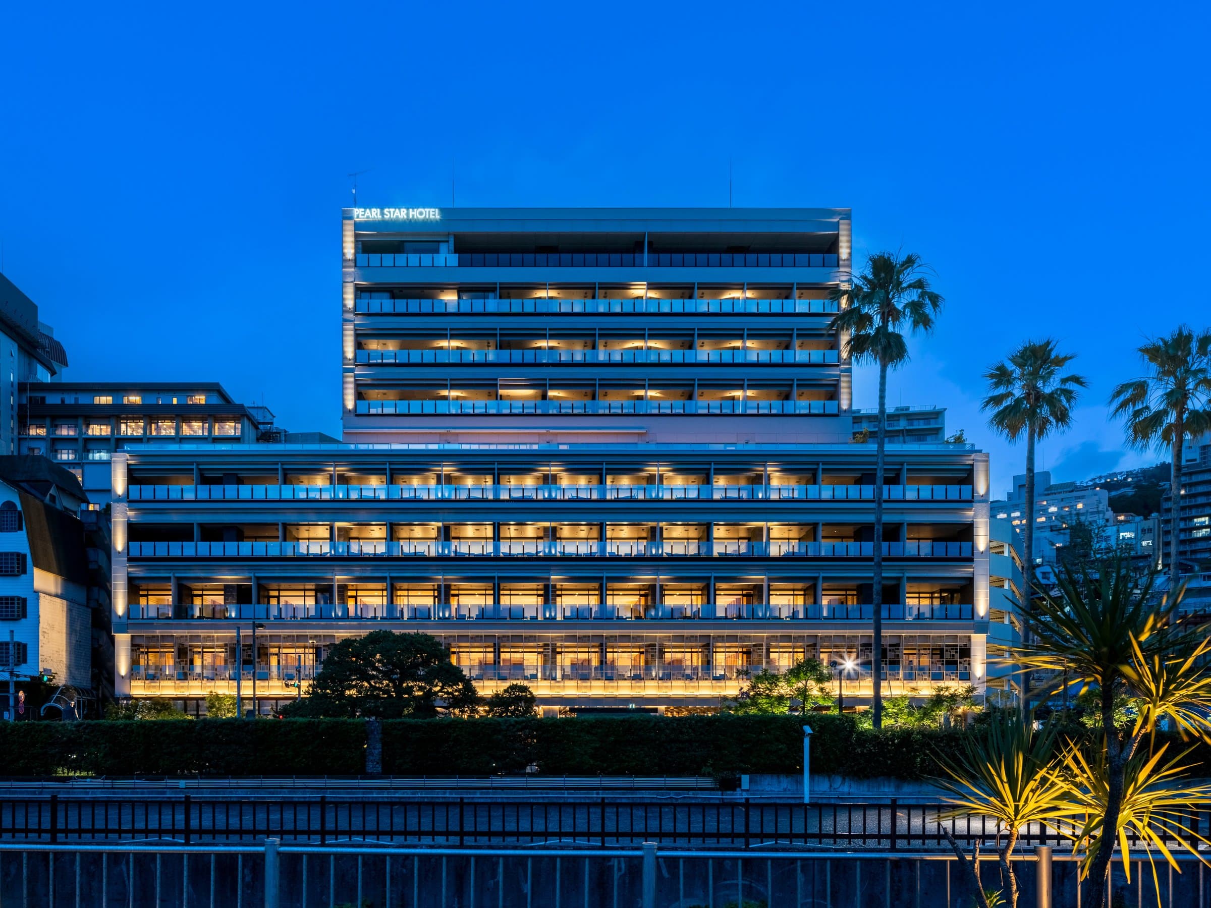 Pearl Star Hotel Atami illuminated seafront facade at blue hour with palm trees, on the bay in Atami Onsen