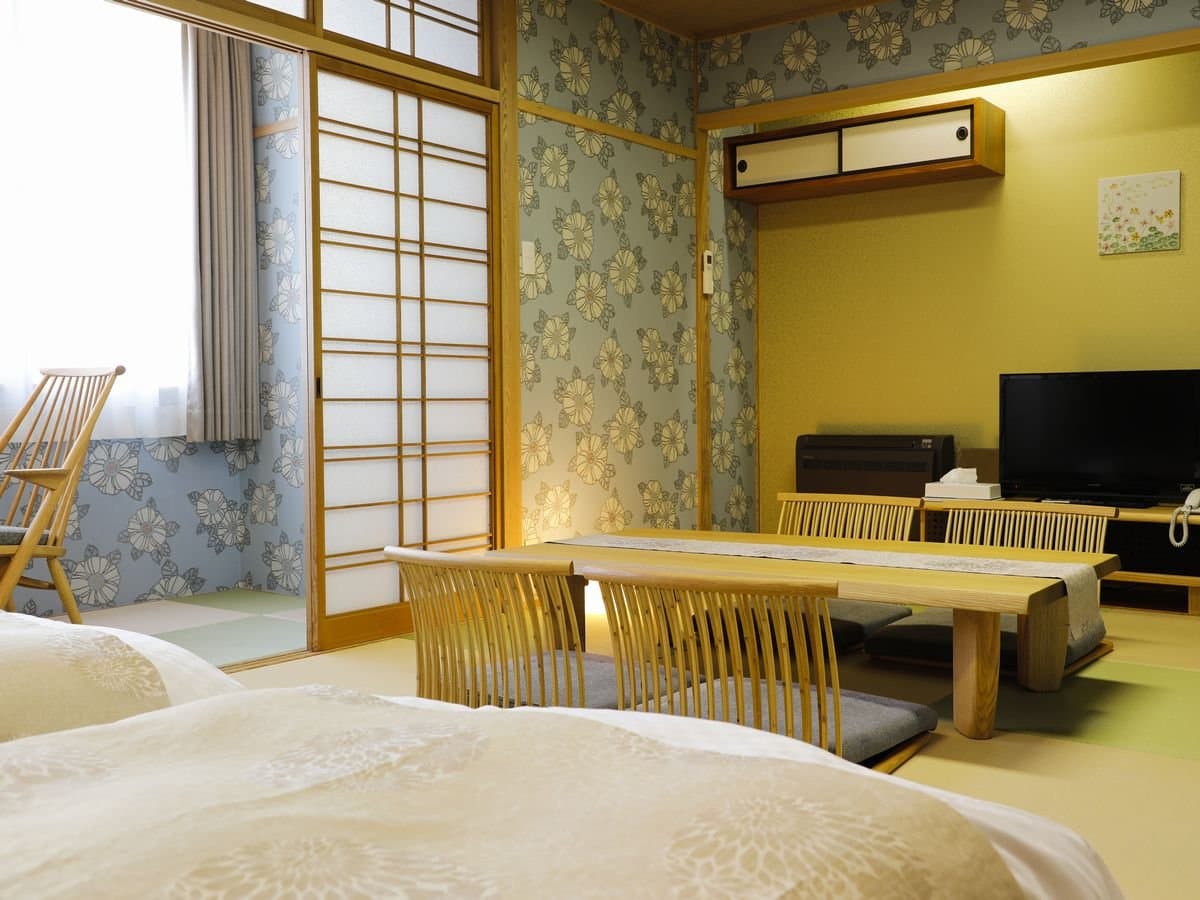 Japanese-style tatami guest room with futon bedding, low table and floral wall accents at Hotel Katsuragi, Dogo Onsen