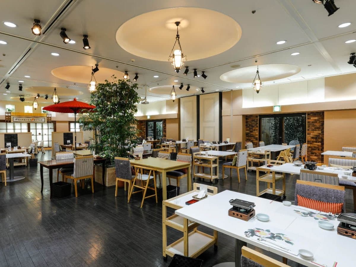 Bright dining hall with pendant lanterns and wooden tables for buffet dinner at Hotel Katsuragi, Dogo Onsen