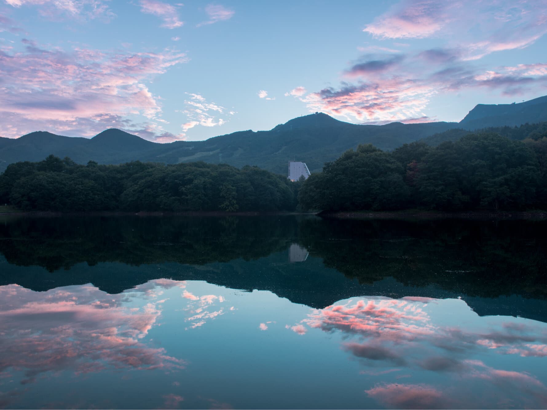 Takamiya Rurikura Resort glowing at dawn beyond a still lake mirroring the pink Zao mountains