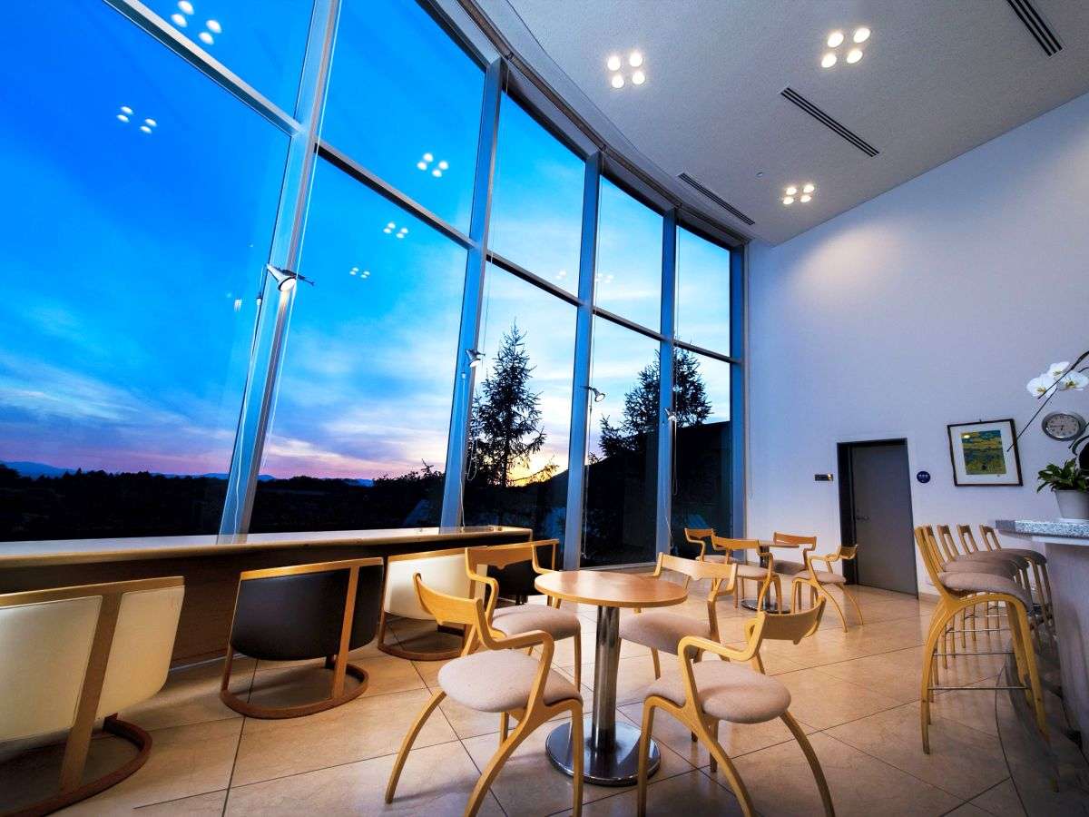 High-ceilinged terrace lounge with a curved glass wall framing a twilight sunset over the Zao valley