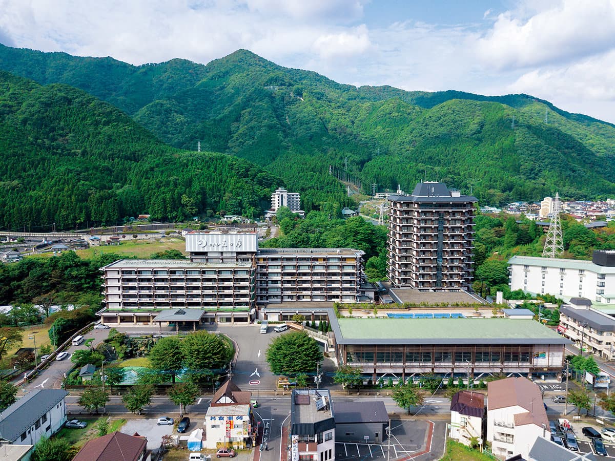 Aerial view of Nikko Kinugawa Hotel Mikazuki's full hot-spring resort building set against forested mountains by the Kinugawa River
