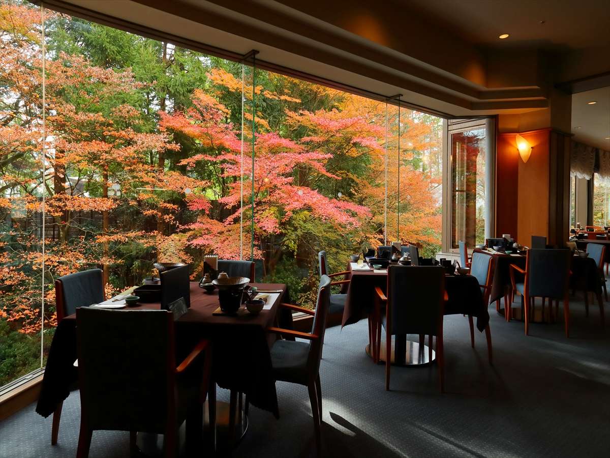 Dining restaurant with table settings and floor-to-ceiling windows framing autumn foliage at Hotel New Mitoya, Akiu Onsen