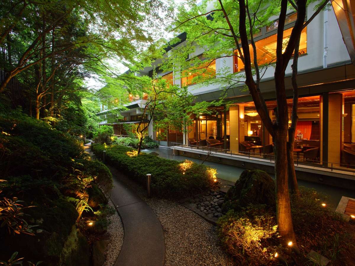 Illuminated garden path leading to the glowing lounge windows of Hotel New Mitoya at dusk, Akiu Onsen