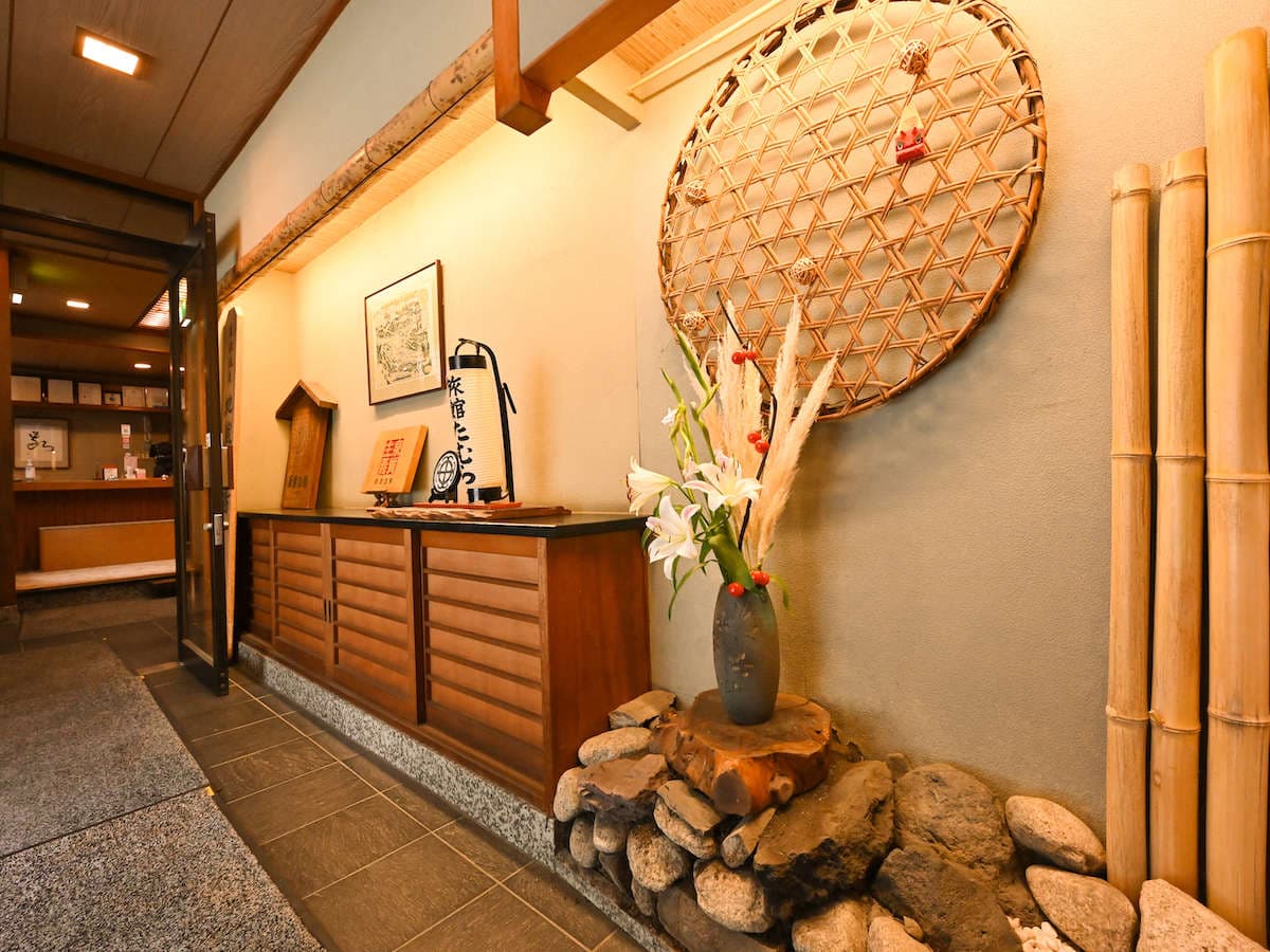 Entrance hallway at Ryokan Tamura with a lily ikebana arrangement and a woven bamboo wall ornament