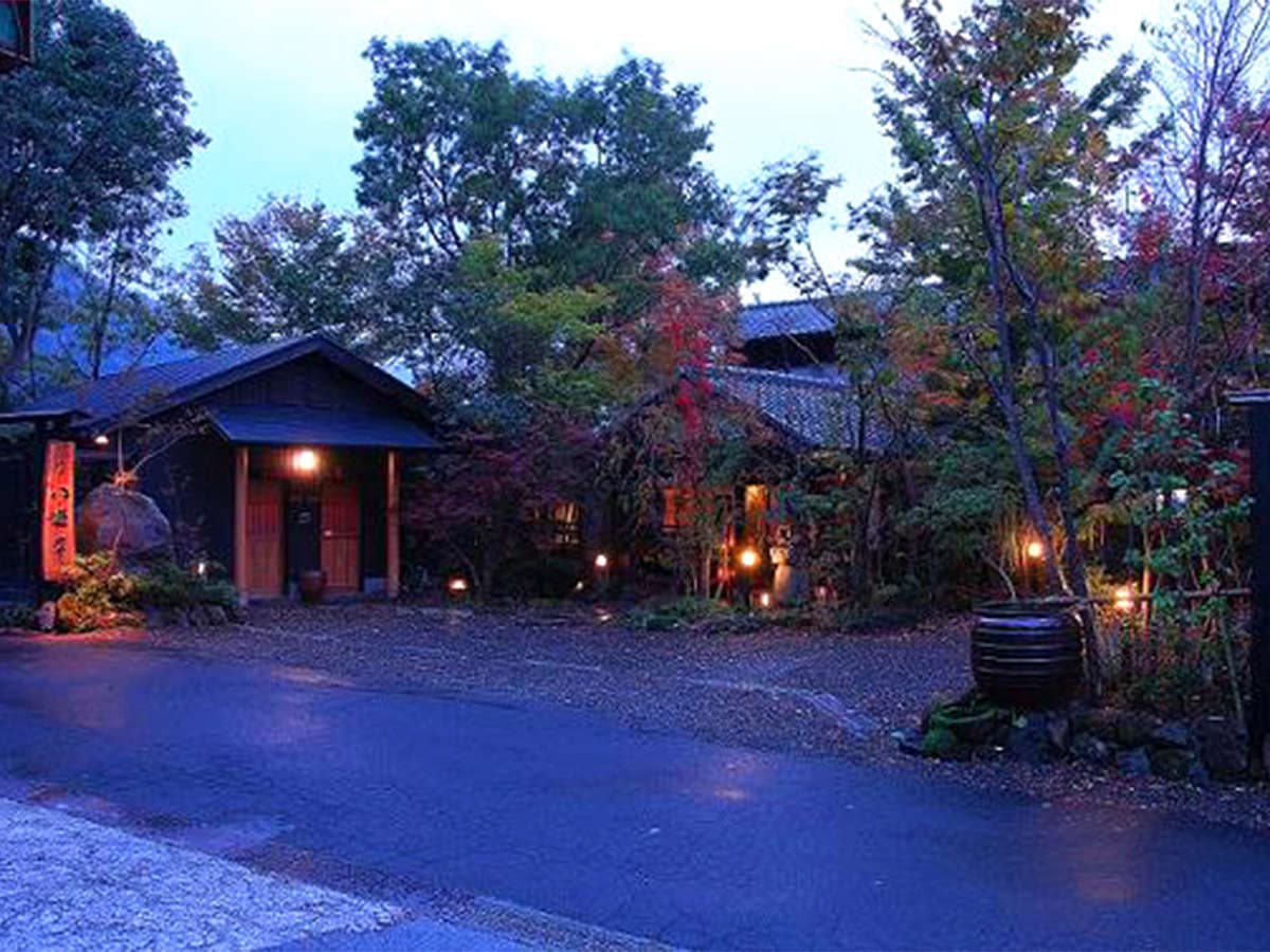 Full exterior of Onjuku Yagura at dusk, dark timber buildings and lantern-lit garden approach in Yufuin