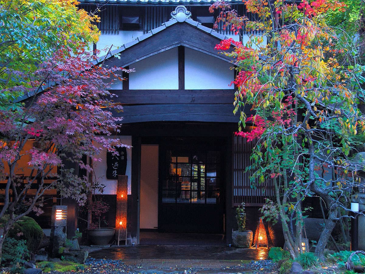 Onjuku Yagura ryokan entrance framed by red autumn maple leaves and lit lanterns in Yufuin Onsen
