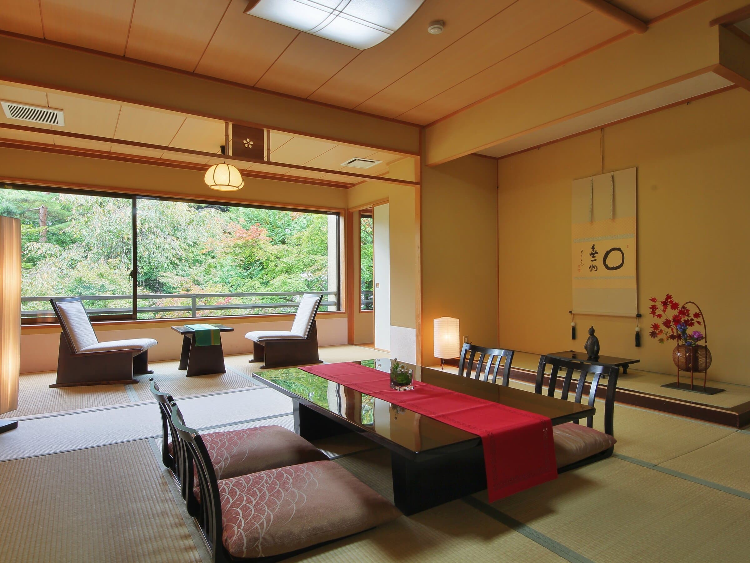 Spacious tatami guest room at Nikko Hoshi no Yado with hanging scroll, low table and garden view through wide windows