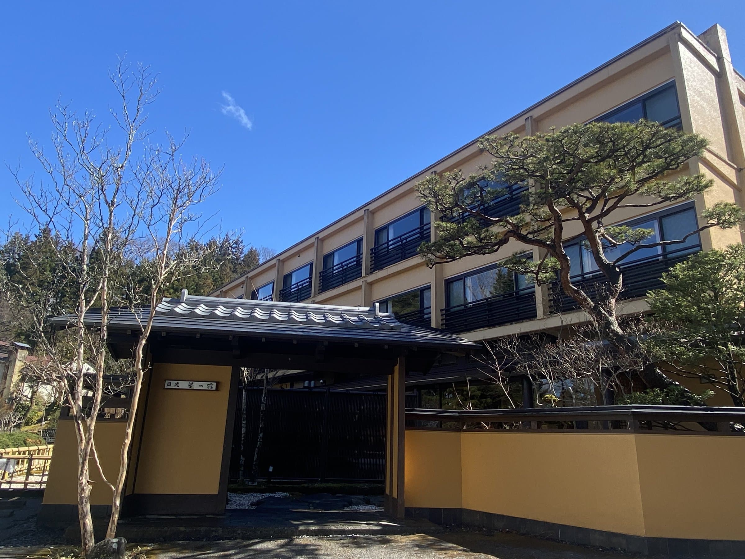 Nikko Hoshi no Yado ryokan exterior with tiled entrance gate, pine tree and main building under blue sky in Nikko